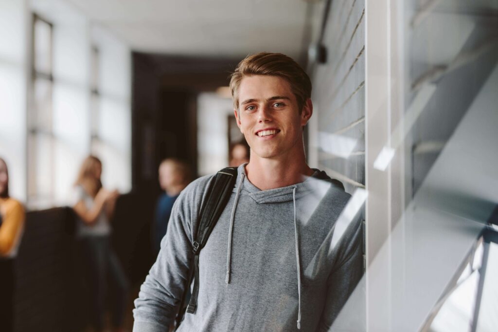Young man with backpack in school hallway smiling